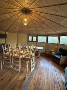 Espace repas intérieur du Domaine des Sens : salle ronde en bois, grande table et baies vitrées sur la chênaie